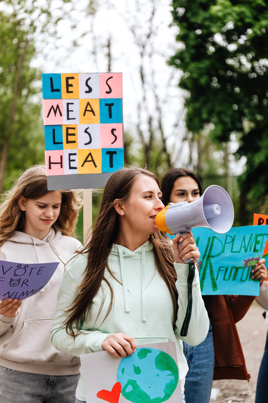 An activist talking into a megaphone and holding a handmade collage of the earth in front of several other people holding signs.