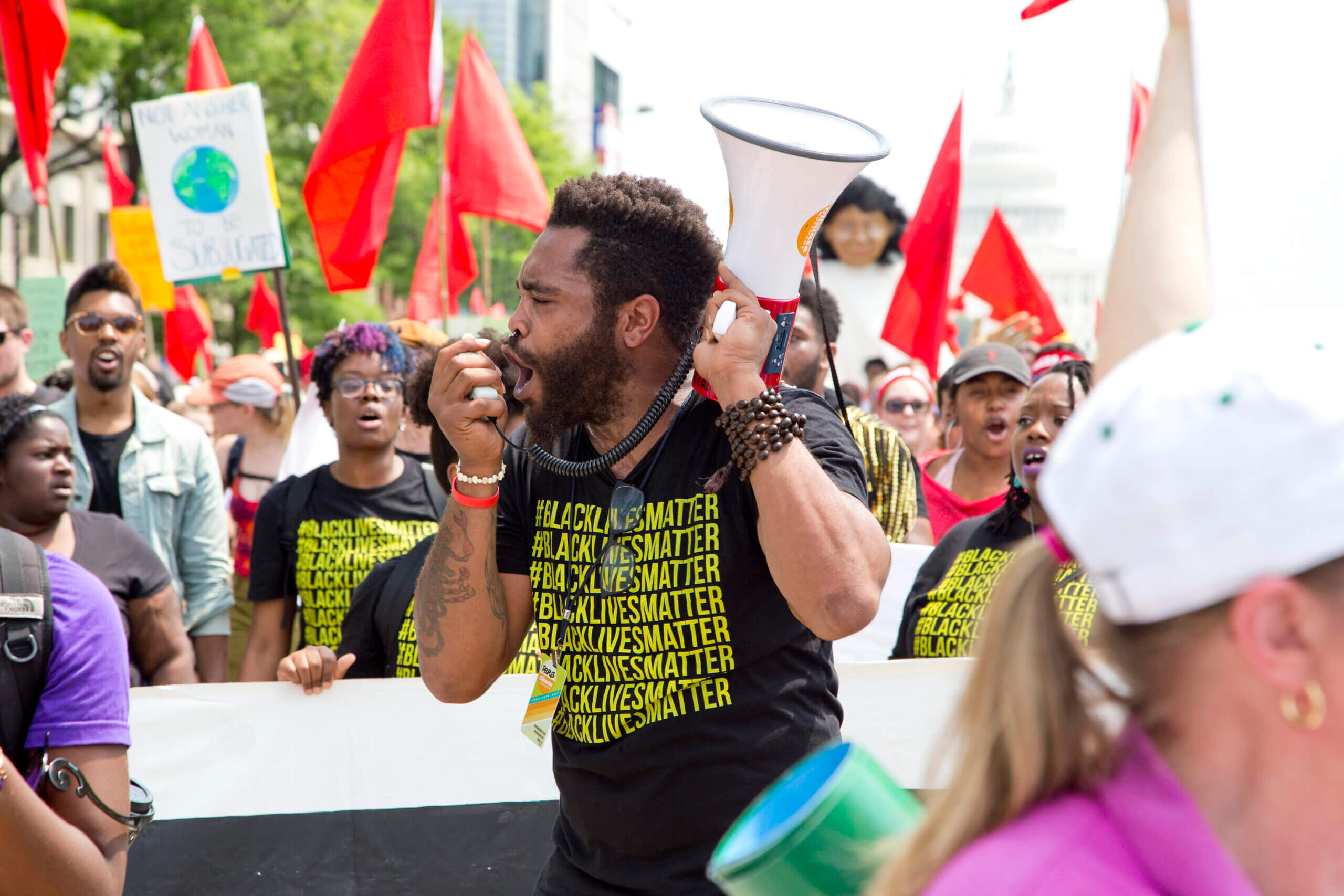 a black man at a protest chanting into a megaphone wearing a black Black Lives Matter shirt