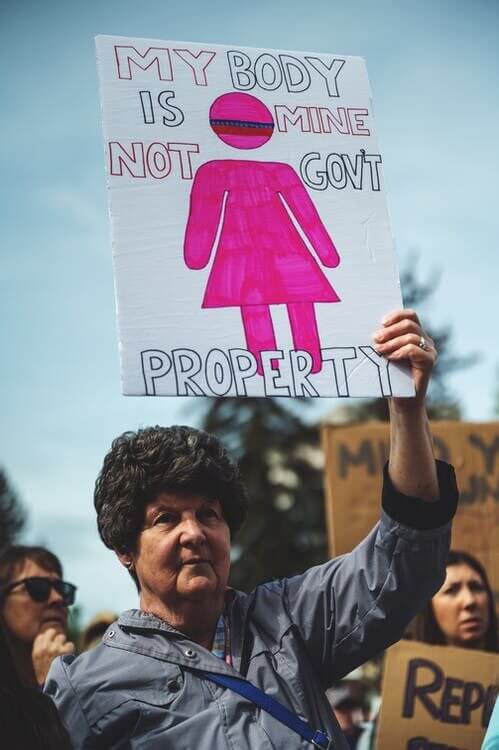 an older white woman holding a homemade sign reading My Body is Mine Not Government Property