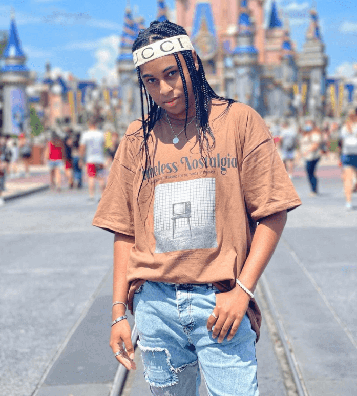 Roy standing in front of Disney castle wearing a khaki colored t shirt and light wash jeans.