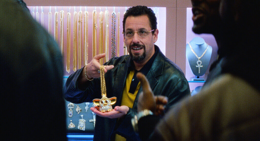 Adam Sandler in Uncut Gems, holding up a blinged out necklace in a jewelry store